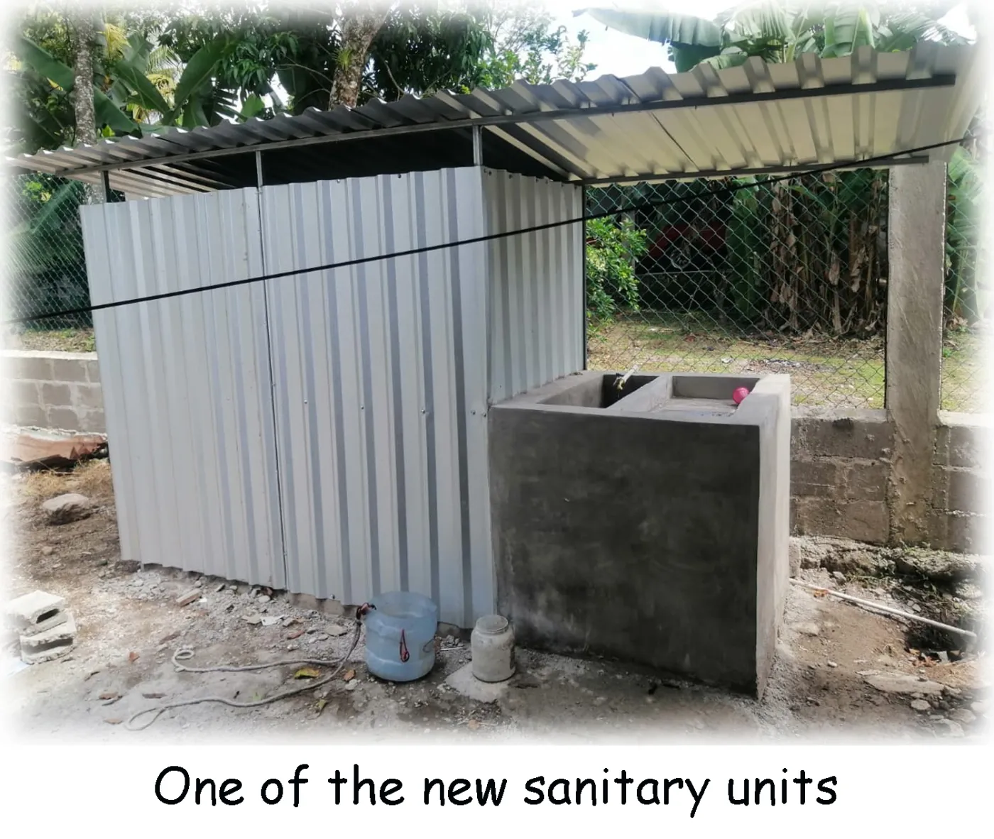 A newly built outdoor sanitary unit with metal privacy stalls and a concrete basin.